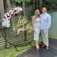 A man and woman posing joyfully next to a neon "Let's Party" sign.