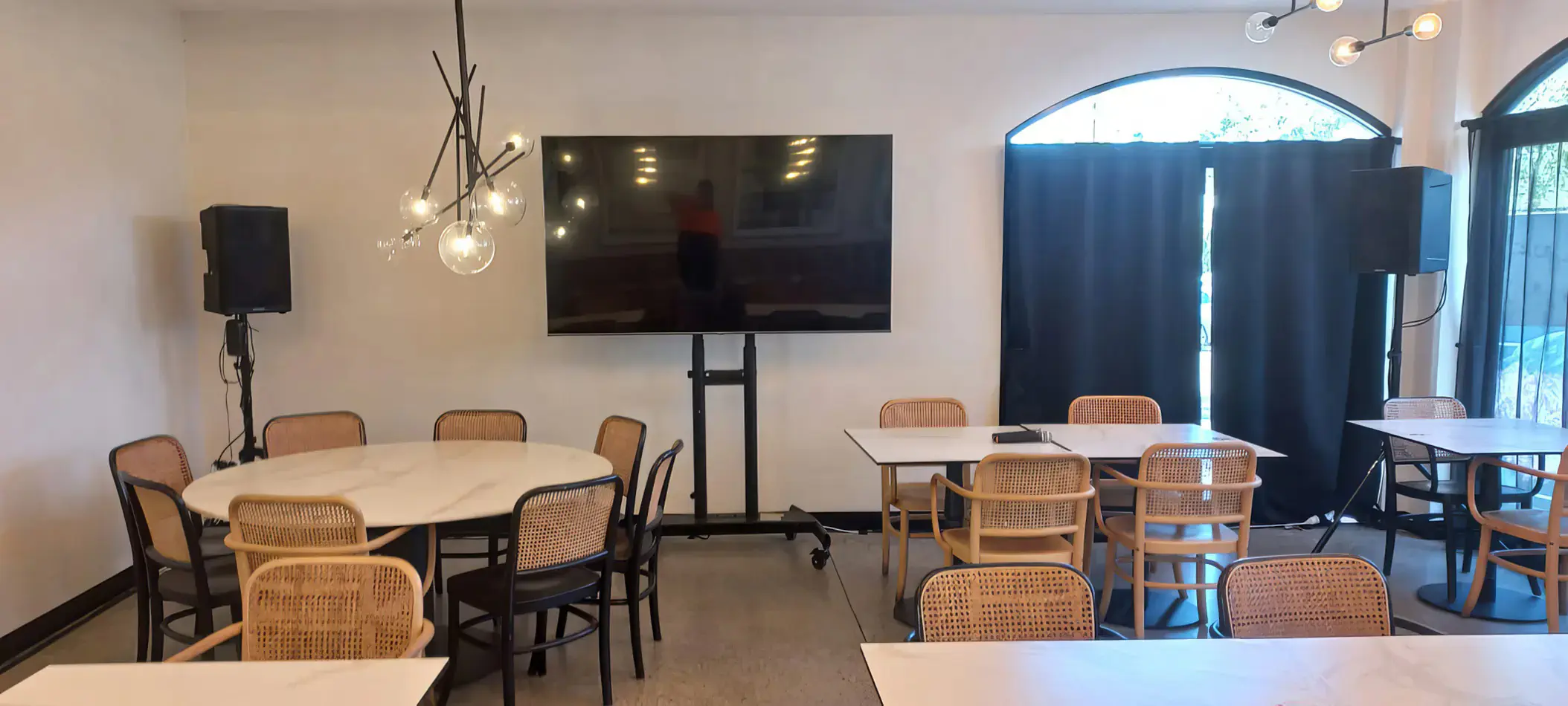Indoor dining space with tables and chairs, TV display on stand, and PA speakers positioned for small event or presentation