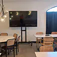 Indoor dining space with tables and chairs, TV display on stand, and PA speakers positioned for small event or presentation