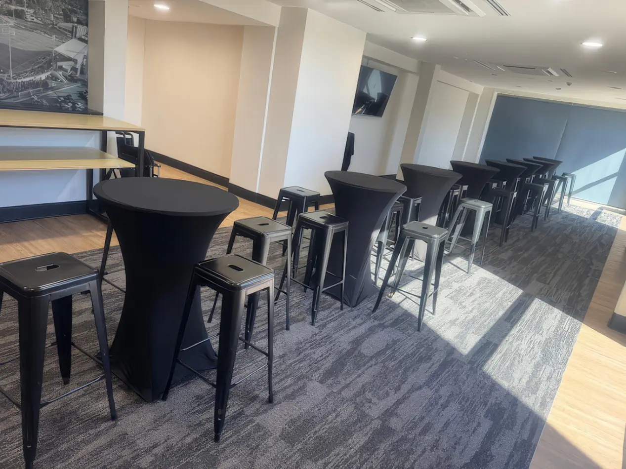 Indoor event setup with black tolix stools and cocktail tables arranged in a modern function room with carpet flooring and natural light
