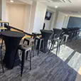 Indoor event setup with black tolix stools and cocktail tables arranged in a modern function room with carpet flooring and natural light
