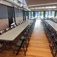 Indoor function venue with long grey trestle tables and black folding chairs arranged for a large event or presentation