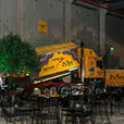 Black wire cocktail tables arranged in a large industrial venue with feature lighting, decorative tree and display trucks in the background