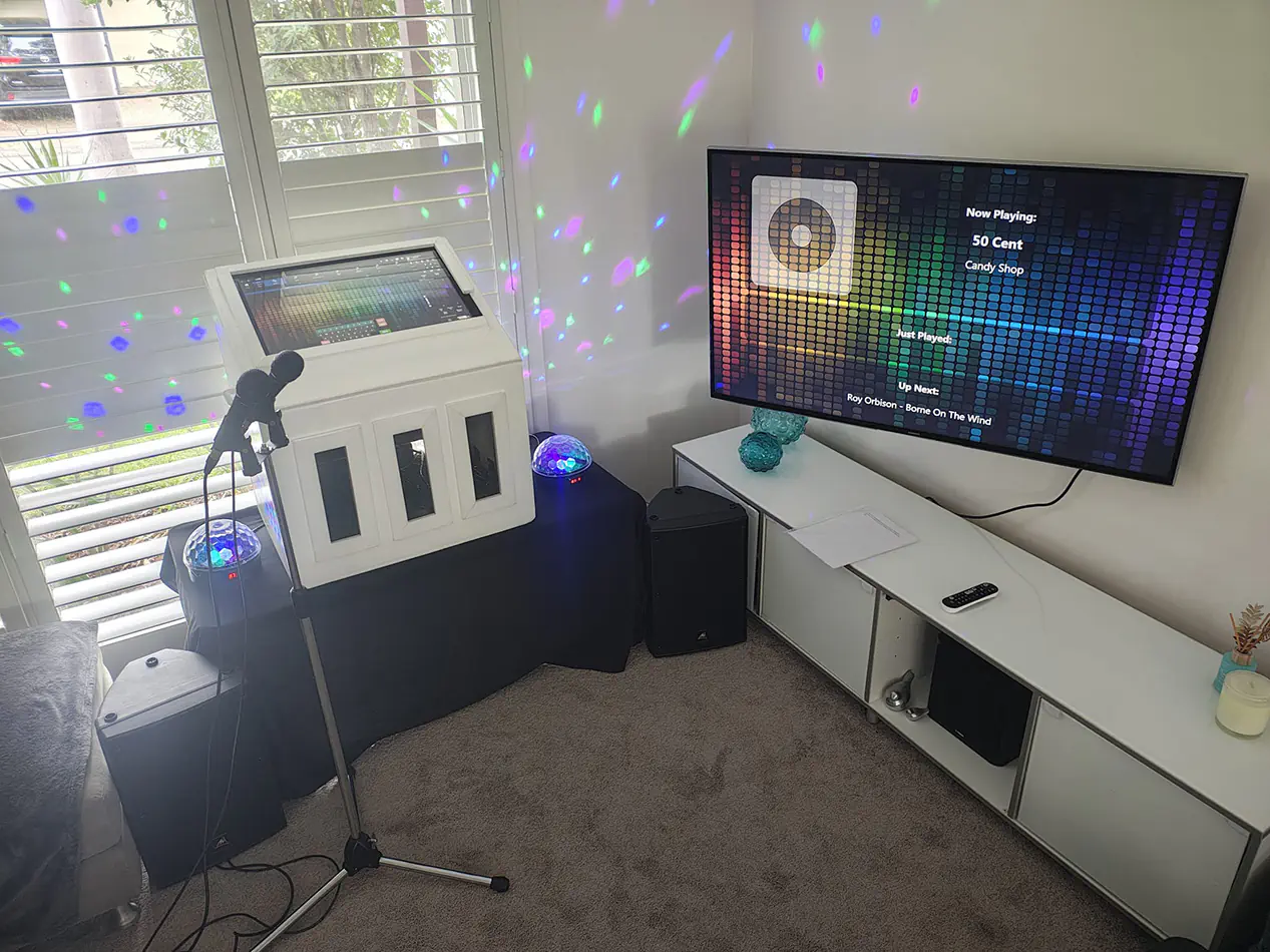 Karaoke machine setup with speakers, microphones and screen displaying music interface in a home environment with coloured party lights