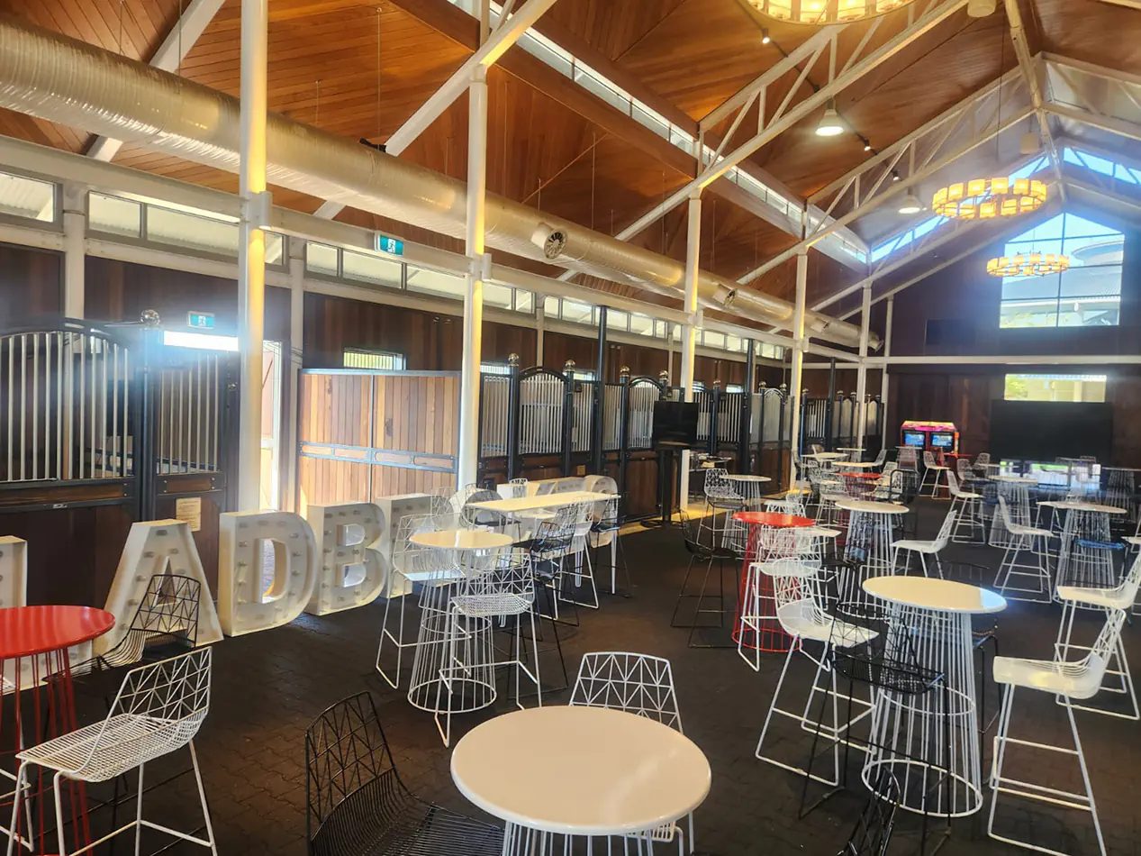 Large indoor venue with wire cocktail tables and matching chairs arranged across a spacious hall with decorative lighting