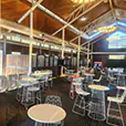Large indoor venue with wire cocktail tables and matching chairs arranged across a spacious hall with decorative lighting