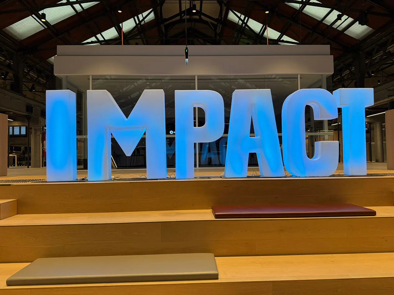 Large illuminated IMPACT event letters glowing blue inside a modern indoor venue space