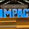 Large illuminated IMPACT event letters glowing blue inside a modern indoor venue space