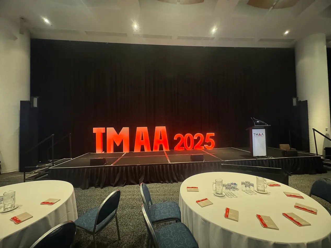 Large illuminated event numbers displaying 2025 on a stage with black backdrop, podium and round dining tables in the foreground