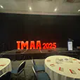 Large illuminated event numbers displaying 2025 on a stage with black backdrop, podium and round dining tables in the foreground