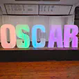 Large illuminated letter sign spelling OSCAR with soft colour lighting set on a stage with curtains and wooden flooring for an event display