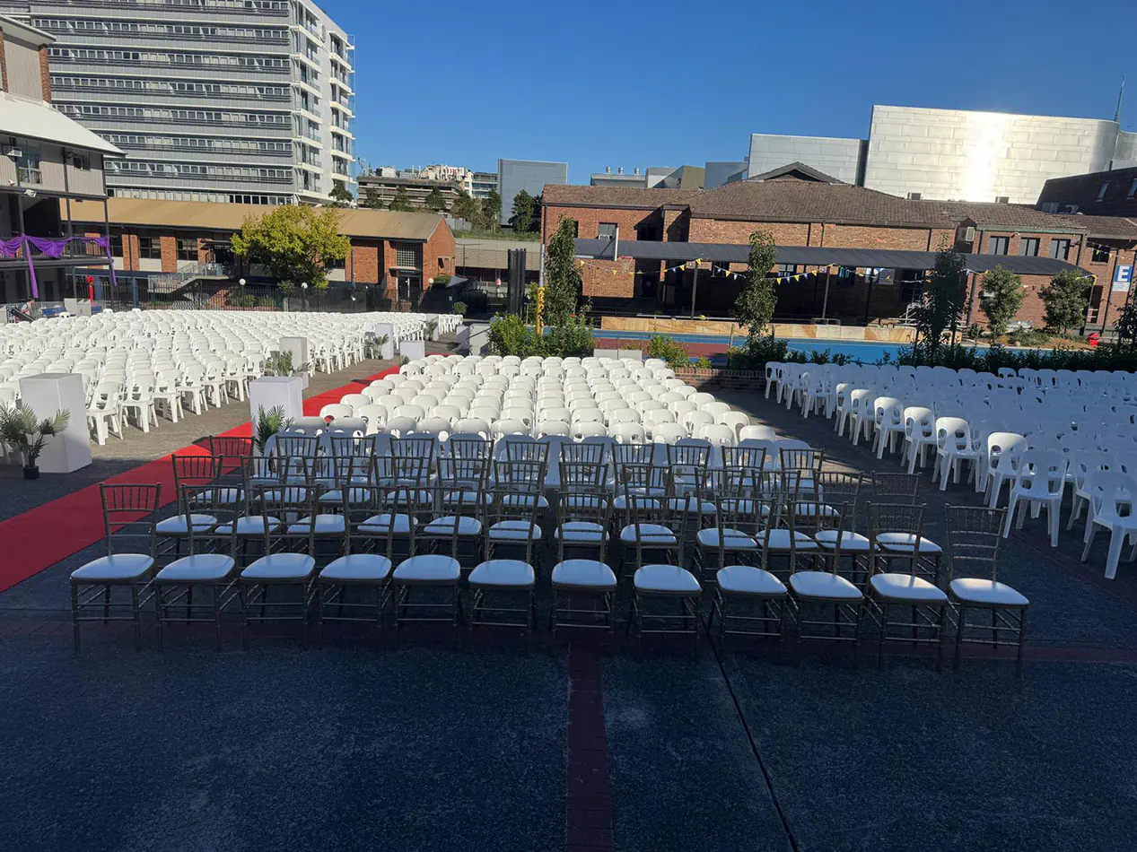 Large outdoor event seating arrangement with rows of white chairs facing a central aisle in an open venue space