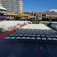 Large outdoor event seating arrangement with rows of white chairs facing a central aisle in an open venue space