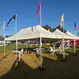 Large white pop-up marquee setup with tables, chairs and colourful flags at a community outdoor event on grass