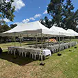 Large white pop-up marquees covering banquet tables and white chairs for an outdoor function in a park setting