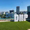 Large white illuminated letters spelling DNP positioned on a rooftop event space overlooking a city skyline with buildings and water views