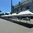Large white pop up marquee set up on paved ground outside a stadium, with weighted legs and multiple market-style marquees in the background