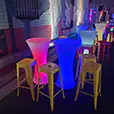 LED glow cocktail tables in vibrant colours including blue, pink, and green set along an outdoor night event space with coloured lighting and bar stools