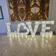 A large light up "LOVE" sign in front of a painting.