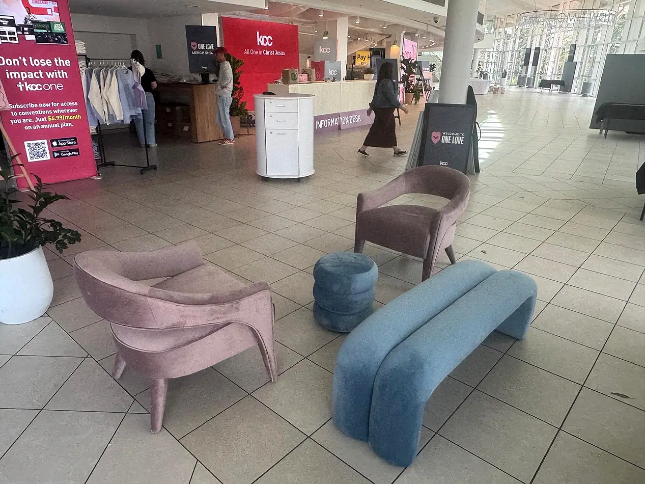 Pink velvet Lola arm chair set up in a conference foyer alongside a sky blue Apollo bench seat and ottoman.
