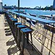 Long bar height table with black stools set up along a waterfront location overlooking Sydney Harbour with boats and bridge views in the background