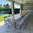 Long timber banquet table with black hairpin legs and white folding chairs on a covered outdoor entertaining patio