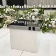 Mirror gloss cake table with reflective black surface, surrounded by lush white and green floral arrangements and rows of tall candles at a wedding reception.