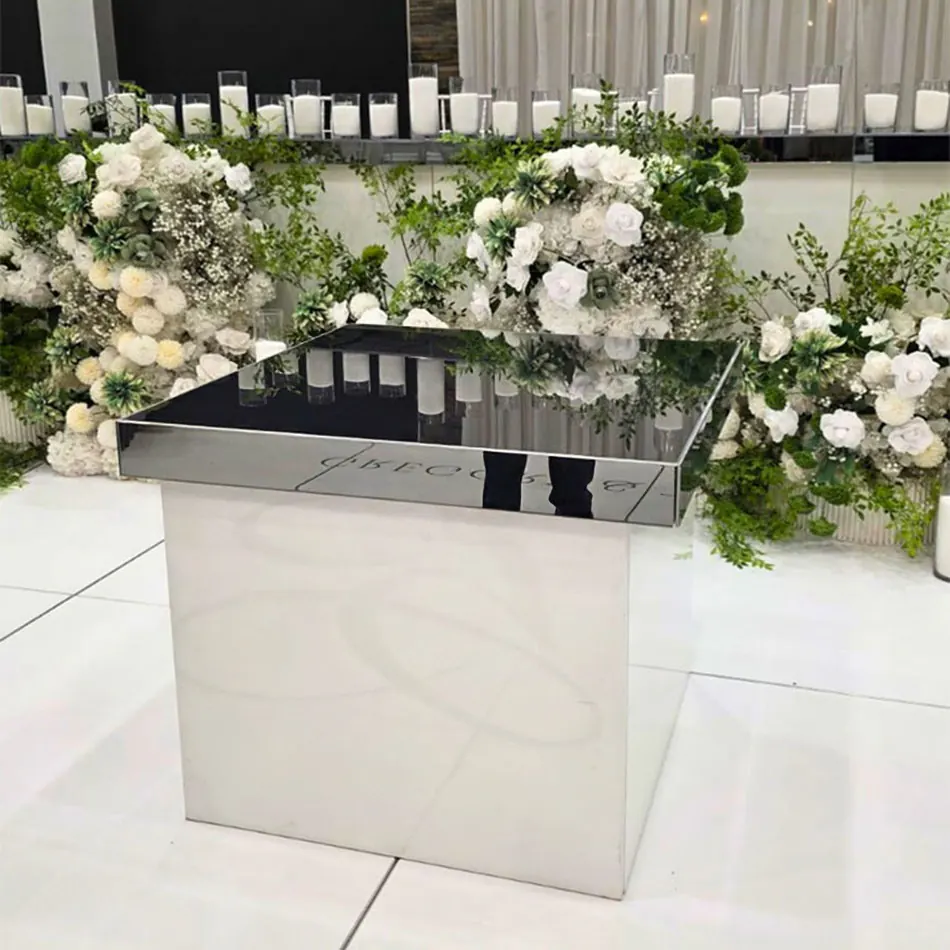 Mirror gloss cake table with reflective black surface, surrounded by lush white and green floral arrangements and rows of tall candles at a wedding reception.