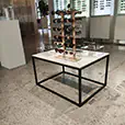 Modern display table with black frame and white top showcasing sunglasses in a retail showroom with illuminated wall displays