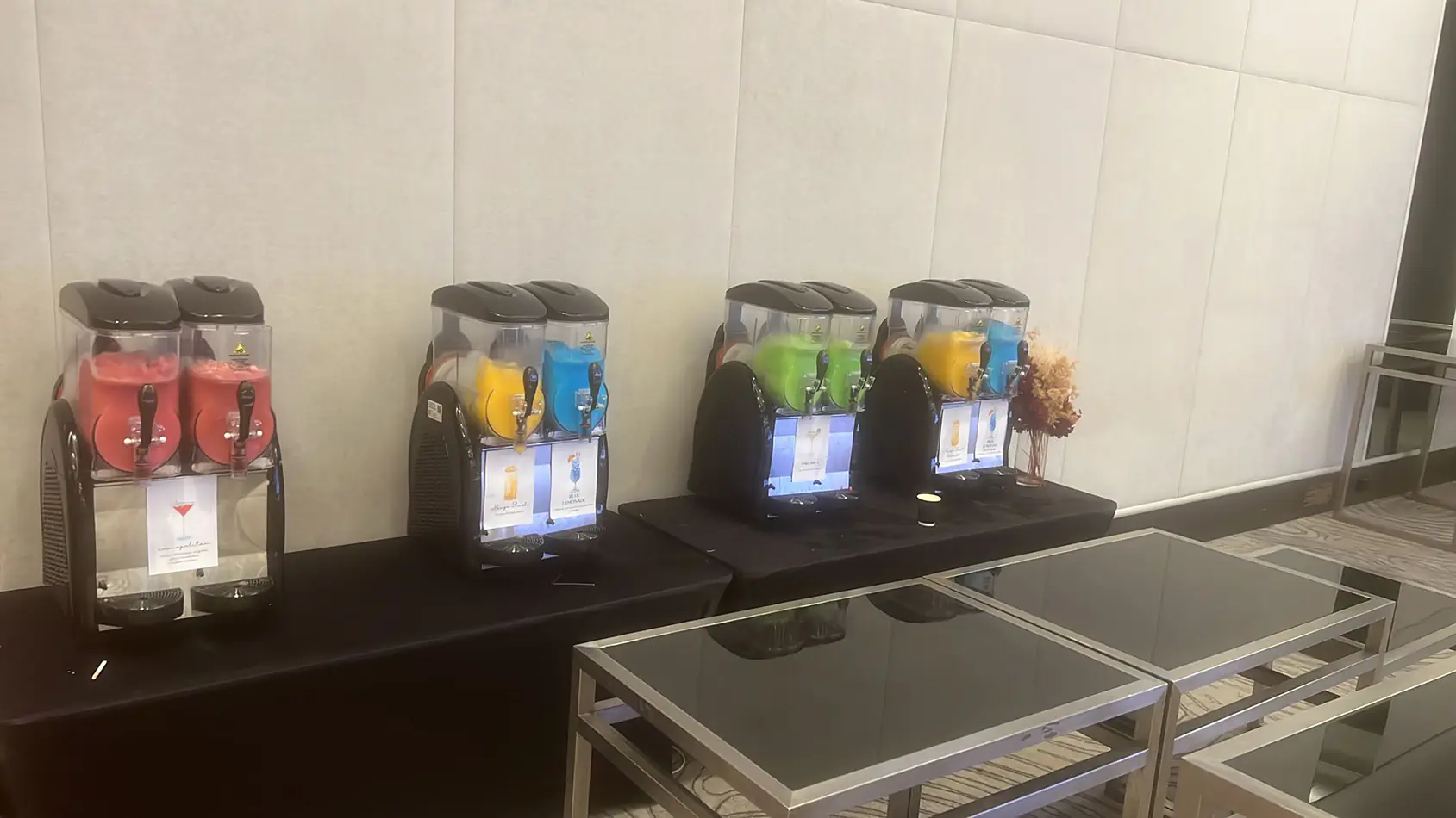 Multiple slushie machines arranged on tables as a refreshment station with different coloured frozen drinks at an event