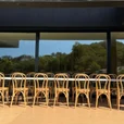 Natural beech bentwood chairs arranged in rows around long white dining tables on a sunny outdoor terrace