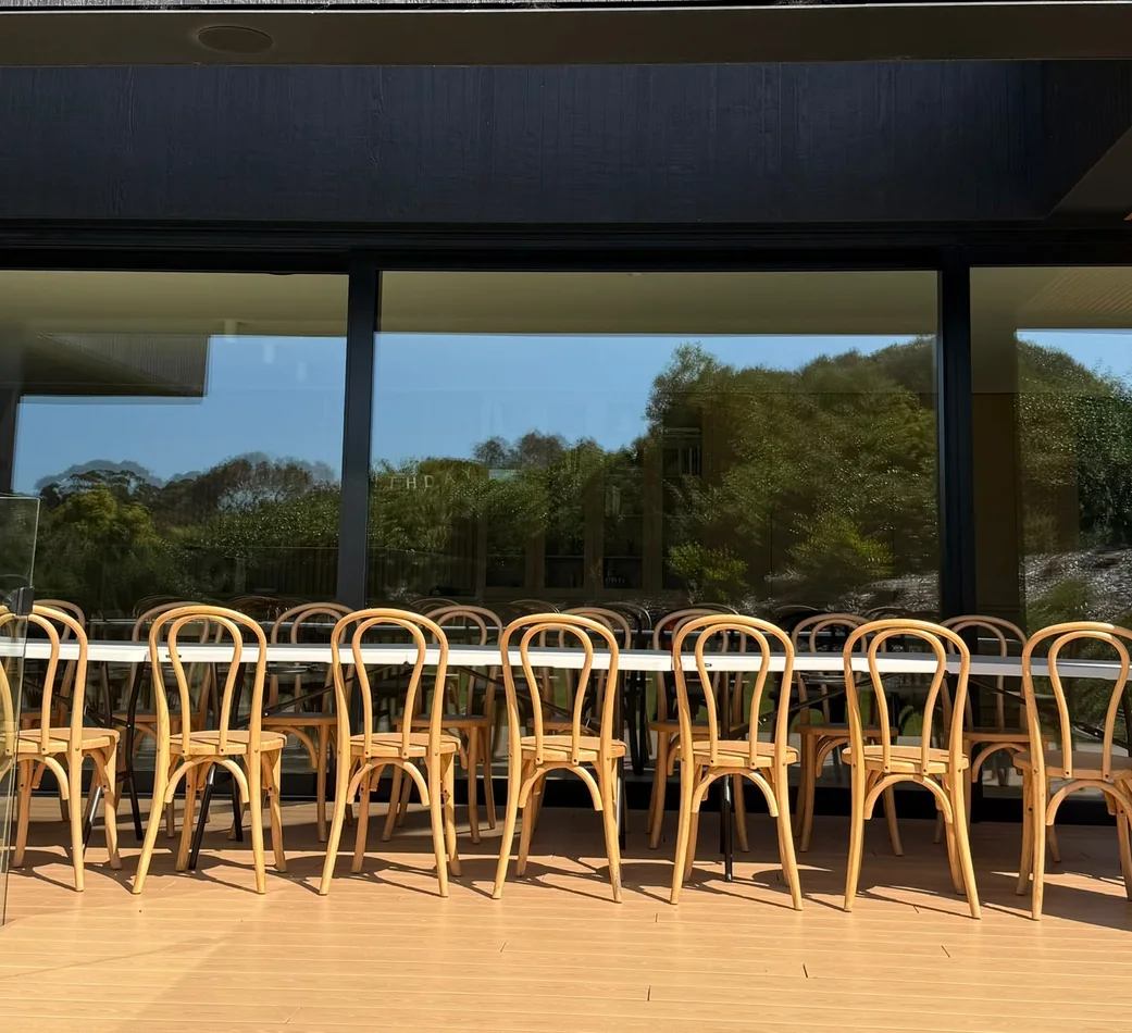 Natural beech bentwood chairs arranged in rows around long white dining tables on a sunny outdoor terrace
