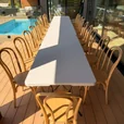 Natural beech bentwood chairs set around a long white dining table beside a residential swimming pool