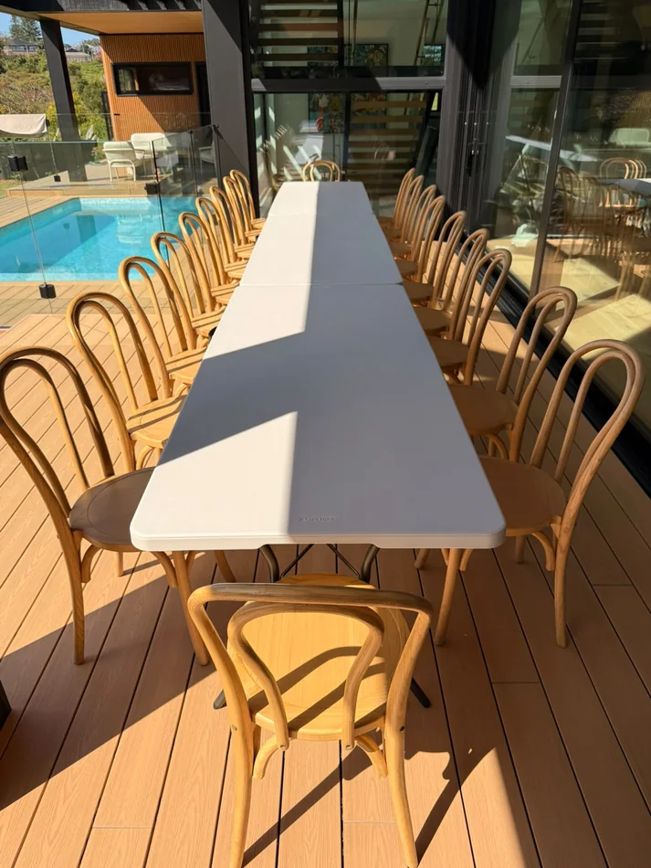 Natural beech bentwood chairs set around a long white dining table beside a residential swimming pool