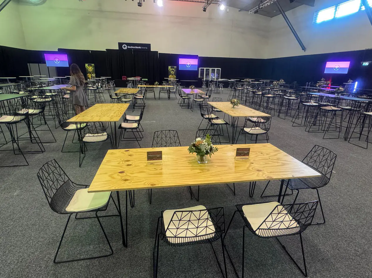 Natural timber hairpin leg tables with black wire event chairs arranged inside a large indoor function venue