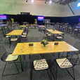 Natural timber hairpin leg tables with black wire event chairs arranged inside a large indoor function venue