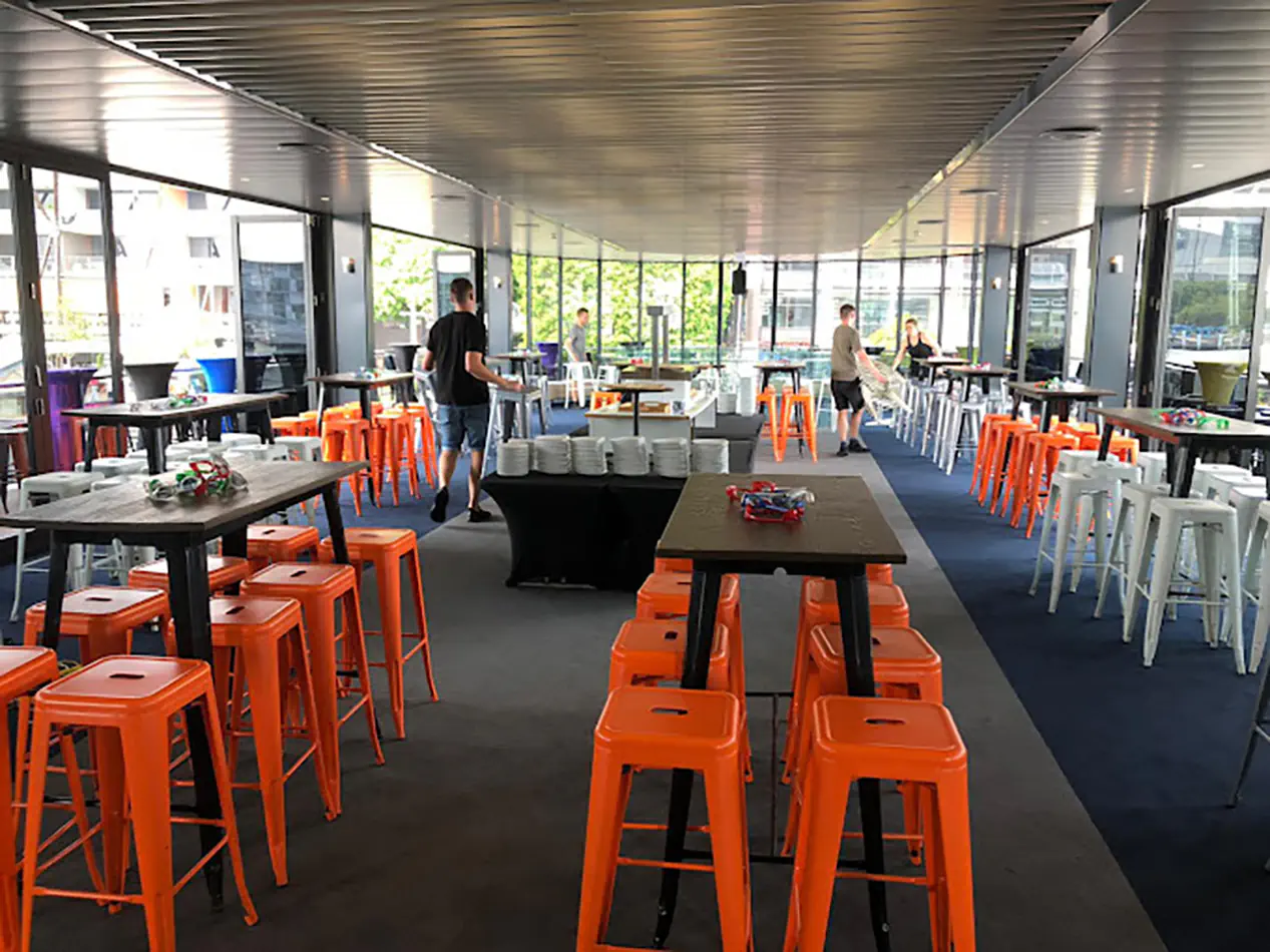 Orange metal bar stools arranged around cocktail tables in a modern indoor event venue with high tables and casual seating