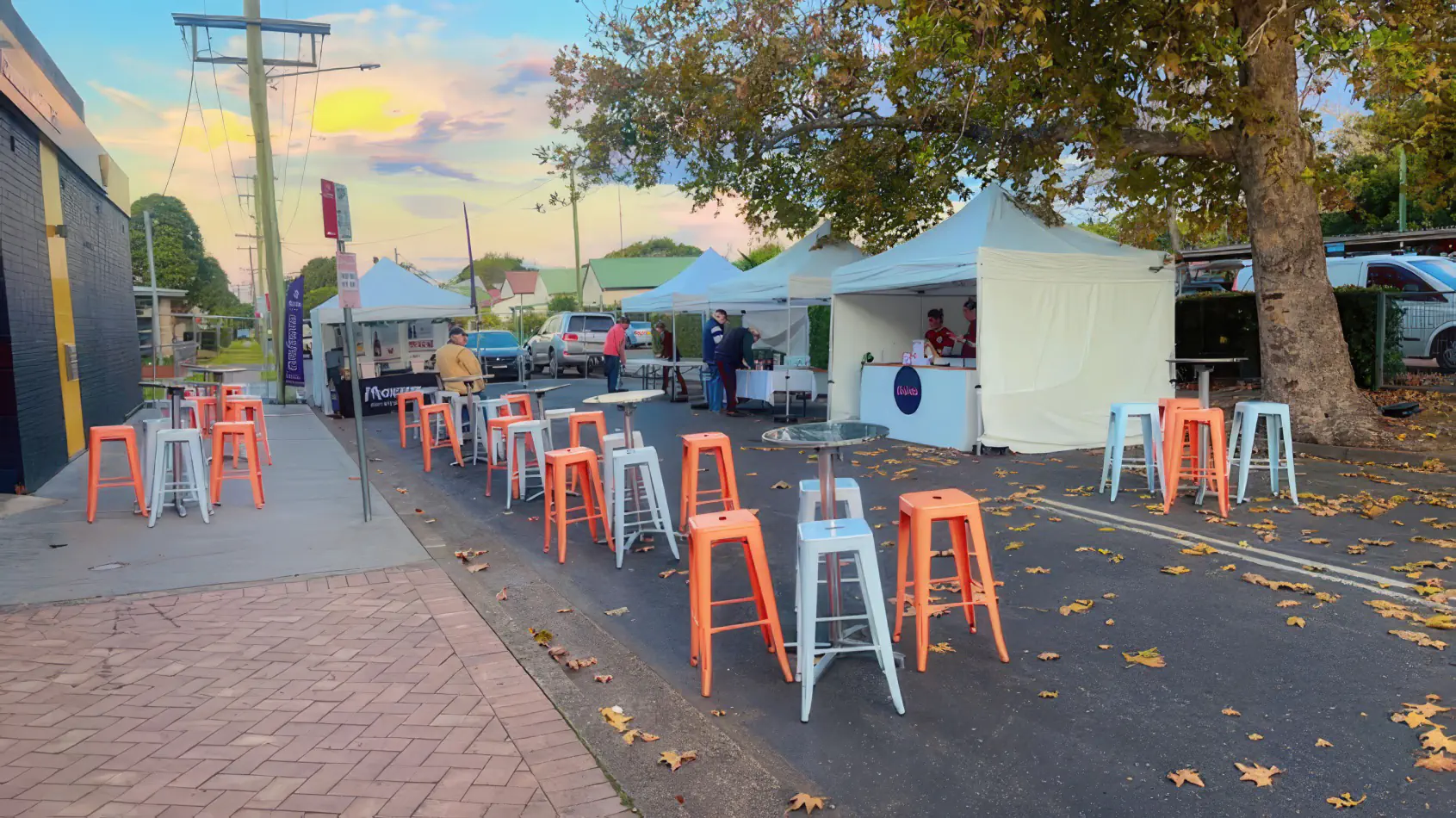 Orange tolix stool hire mixed with white stools and cocktail tables at an outdoor street market event with vendor tents and casual seating setup