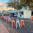 Orange tolix stool hire mixed with white stools and cocktail tables at an outdoor street market event with vendor tents and casual seating setup