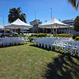 Outdoor ceremony setup with white pop-up marquees and rows of white chairs arranged on grass near a transport precinct