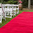 Outdoor ceremony setup with red carpet aisle, garden surroundings, floral arrangement, and guest seating for a formal event