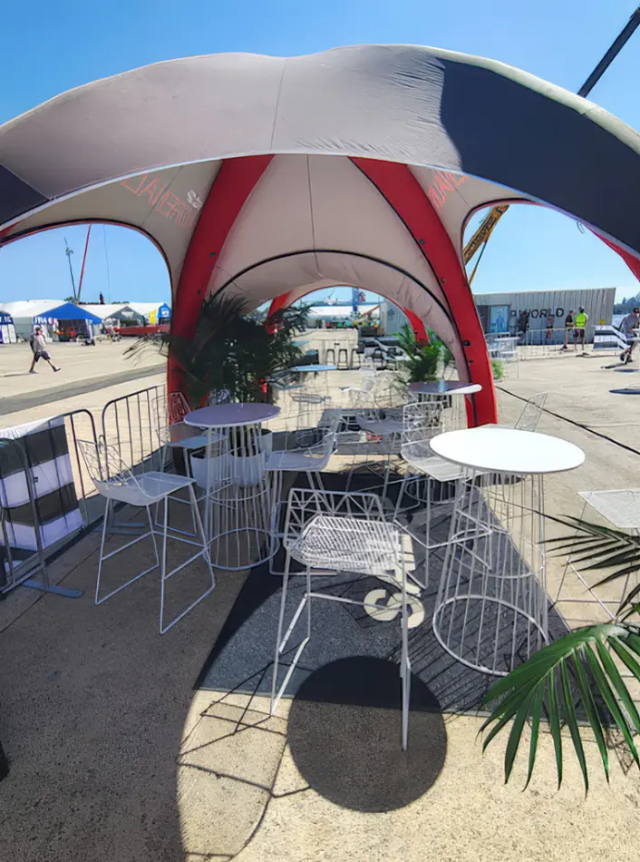 White wire cocktail tables and matching stools arranged at an outdoor event setup with open surroundings and coastal backdrop