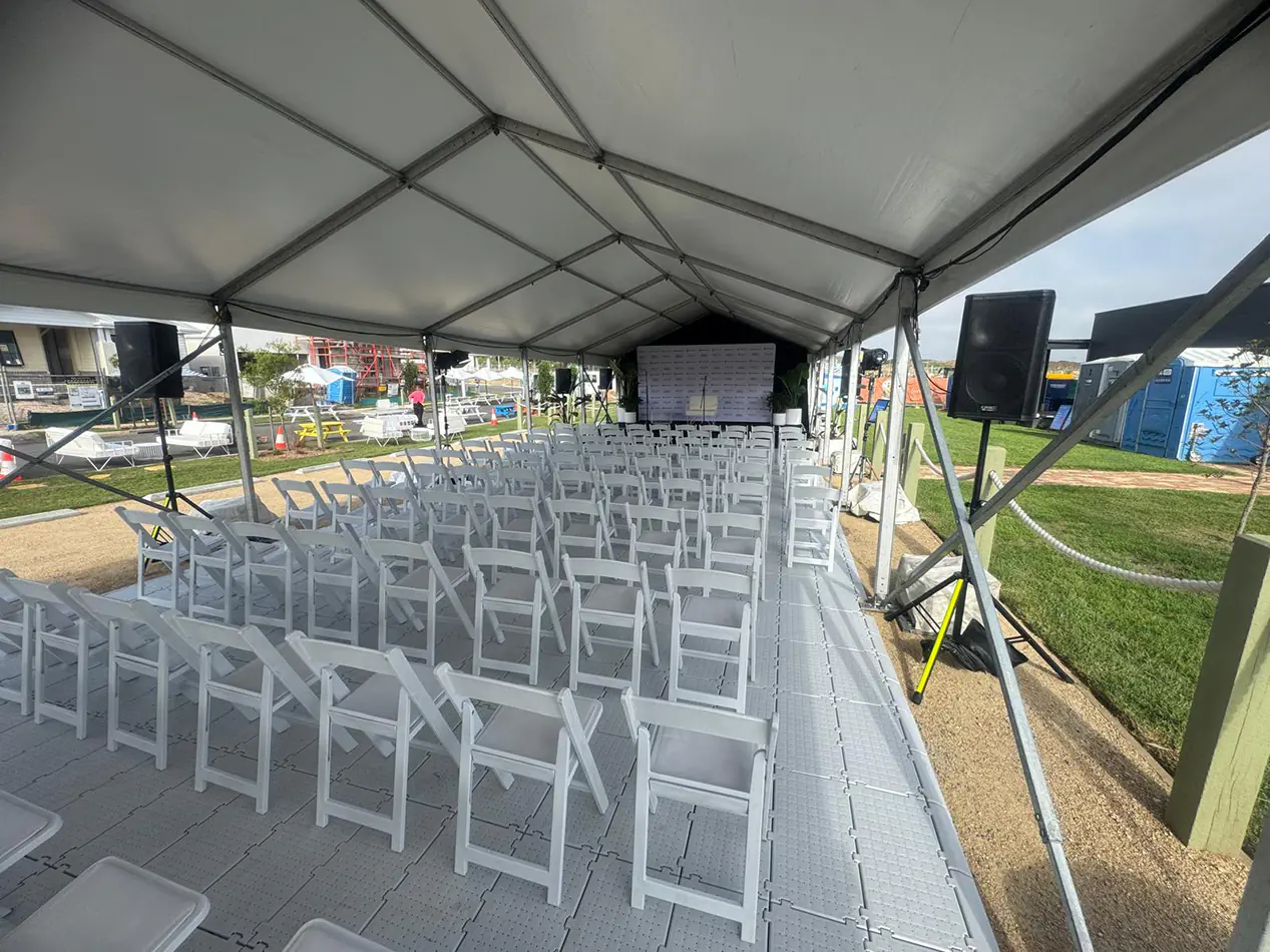 Outdoor event presentation setup with PA speaker system, projection screen, and rows of guest seating inside a covered event structure