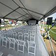 Outdoor event presentation setup with PA speaker system, projection screen, and rows of guest seating inside a covered event structure