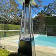 Outdoor pyramid gas heater beside a pool and landscaped entertaining area with visible flame heating element