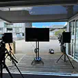 Outdoor event setup with TV screen on stand, speakers on tripods, and camera equipment arranged on timber deck balcony