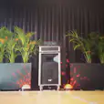 A stage with a speaker and plants in front of it, available for Jukebox Hire Only.