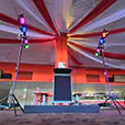 Event stage setup with podium and microphone, featuring par can lighting on stands casting colourful red, blue, and green lights with draped ceiling fabric in a function venue