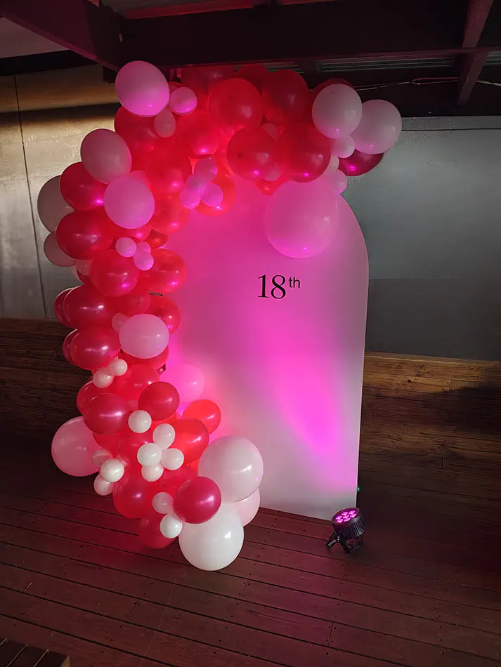 Pink and white balloon display with coloured uplighting and illuminated backdrop for an 18th birthday event