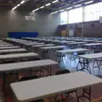 A large gymnasium filled with plastic tables and chairs.